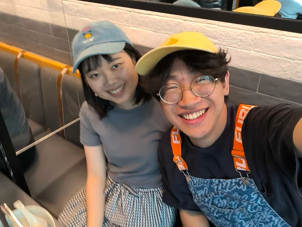 Two people in colourful caps smiling for a selfie in a restaurant booth.