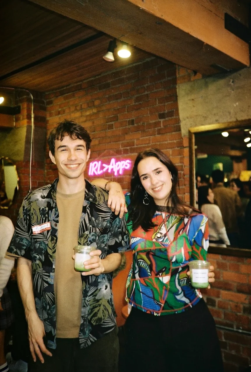 Two smiling people with their arms around each other at a lively evening gathering.